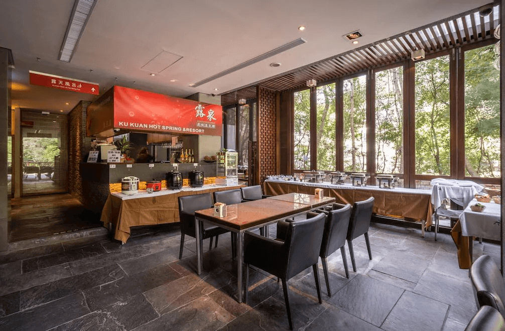 【谷關住宿】露泉渡假溫泉館的早餐餐廳設計挑高並大量採用玻璃窗引入自然光，視野通透。中央設有用餐桌椅區，四周是自助式餐點取用台，包含中式粥品、熱飲與各式熟食，空間舒適溫馨。