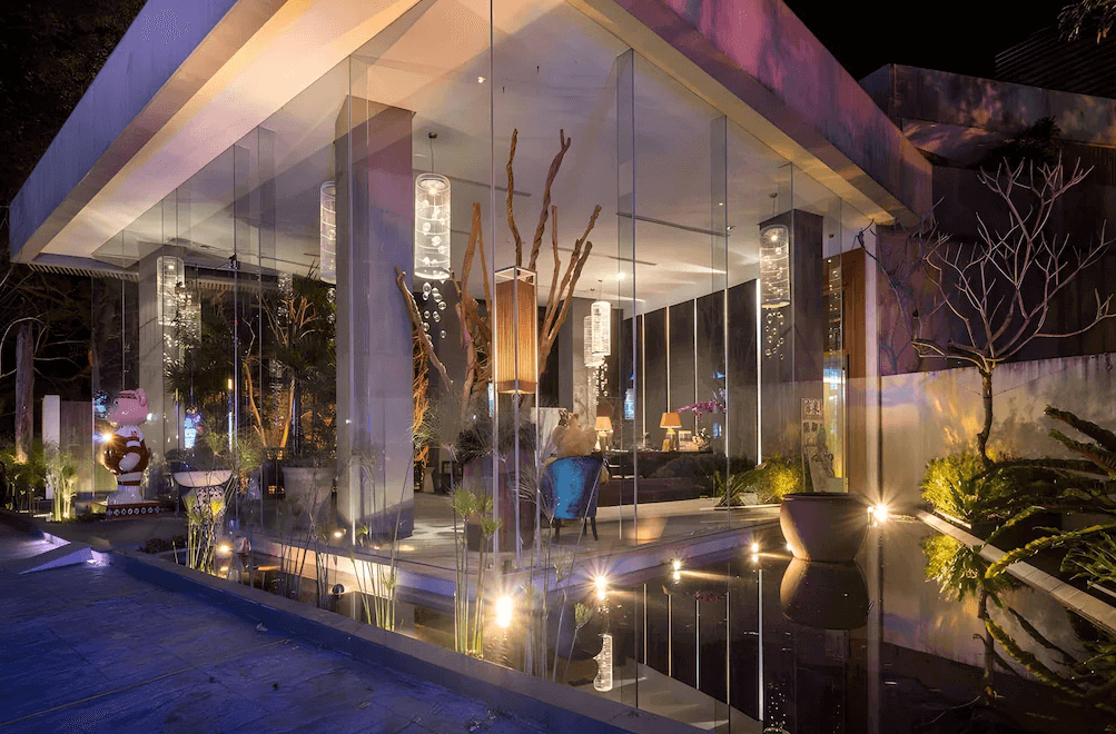 【谷關住宿】露泉渡假溫泉館的玻璃帷幕建築在燈光投射下顯得氣派現代，水池倒影與綠意植栽相互映襯。入口處擺設現代藝術裝置與燈具，夜色中流露出高雅質感與度假氛圍。