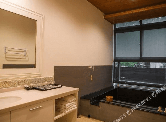 【谷關住宿】麗池山水溫泉會館的湯屋設有黑色石材泡湯池，窗邊即是自然景致，可一邊泡湯一邊欣賞戶外景觀。空間明亮整潔，洗手台與毛巾備品一應俱全，展現典雅與實用兼具的設計。