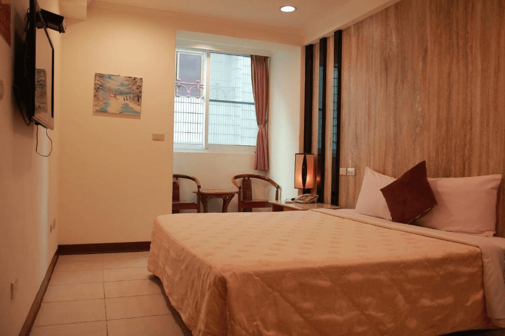 【關子嶺溫泉】“白河住宿”麗湯溫泉渡假山莊的明亮舒適的雙人房，設有柔和燈光與簡約家具，床頭牆為木質紋設計，窗邊設有兩張椅子與小茶几。