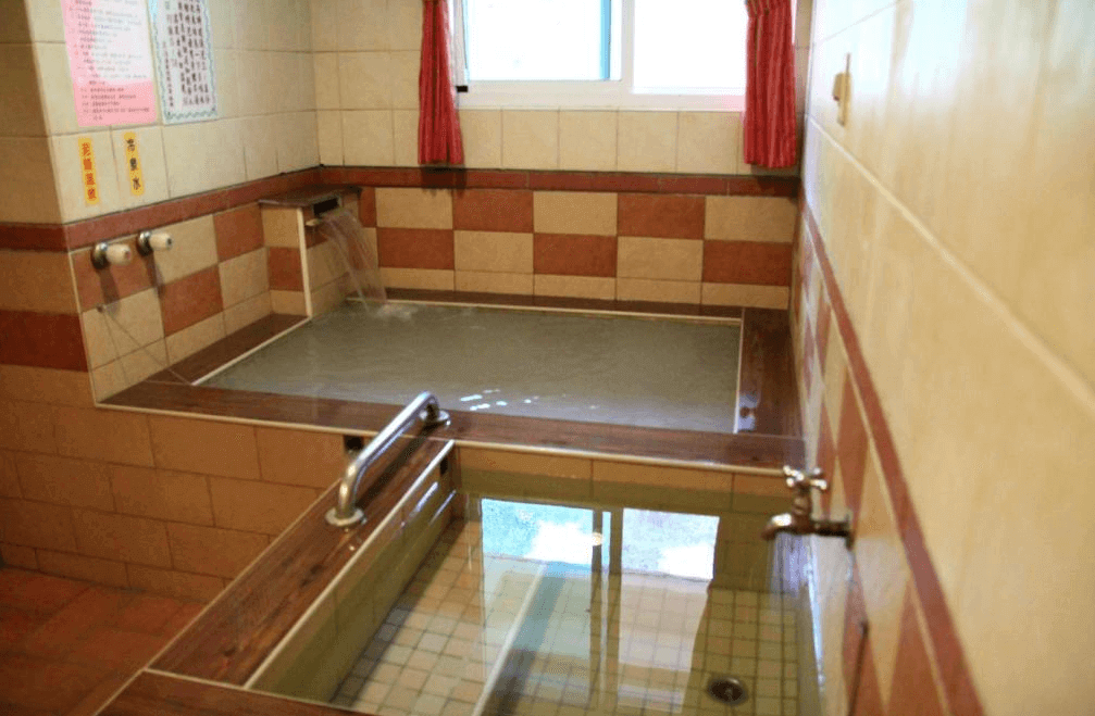 【關子嶺溫泉】“白河住宿”麗湯溫泉渡假山莊備有兩座方形湯池的獨立浴室空間，牆面為紅米色與米色磁磚拼接，設有自然採光窗戶與熱水注水口。