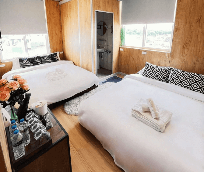 【綠島住宿】20ft 海閣的四人房，木質牆面搭配兩張大床，設有大片窗戶與自然採光，附設乾濕分離衛浴，床上擺放整齊毛巾與抱枕，整體溫馨舒適。