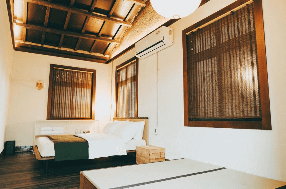 【左營住宿】Goonnight Hostel 軍旅舍復古雙人房，房內設計簡約自然，採木格天花板與深色木窗搭配，雙人床旁配有木箱與簡約床頭燈，呈現懷舊復古風格。