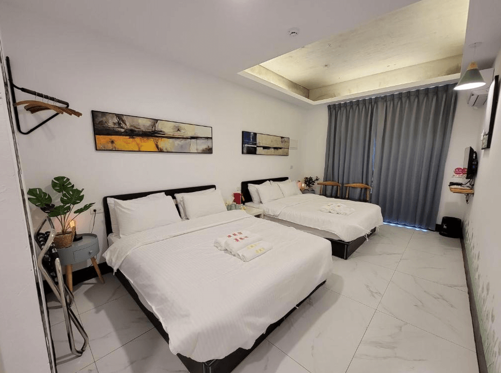 【龍潭住宿】RED ROSE 漫楓宿民宿的家庭房，配有兩張雙人床，白色床單整齊潔淨，牆面掛有抽象畫作增添設計感。房內設有小桌椅、衣架與綠色植栽，空間寬敞明亮，地面為白色大理石瓷磚，窗簾為深灰色遮光布，整體氛圍舒適雅致。