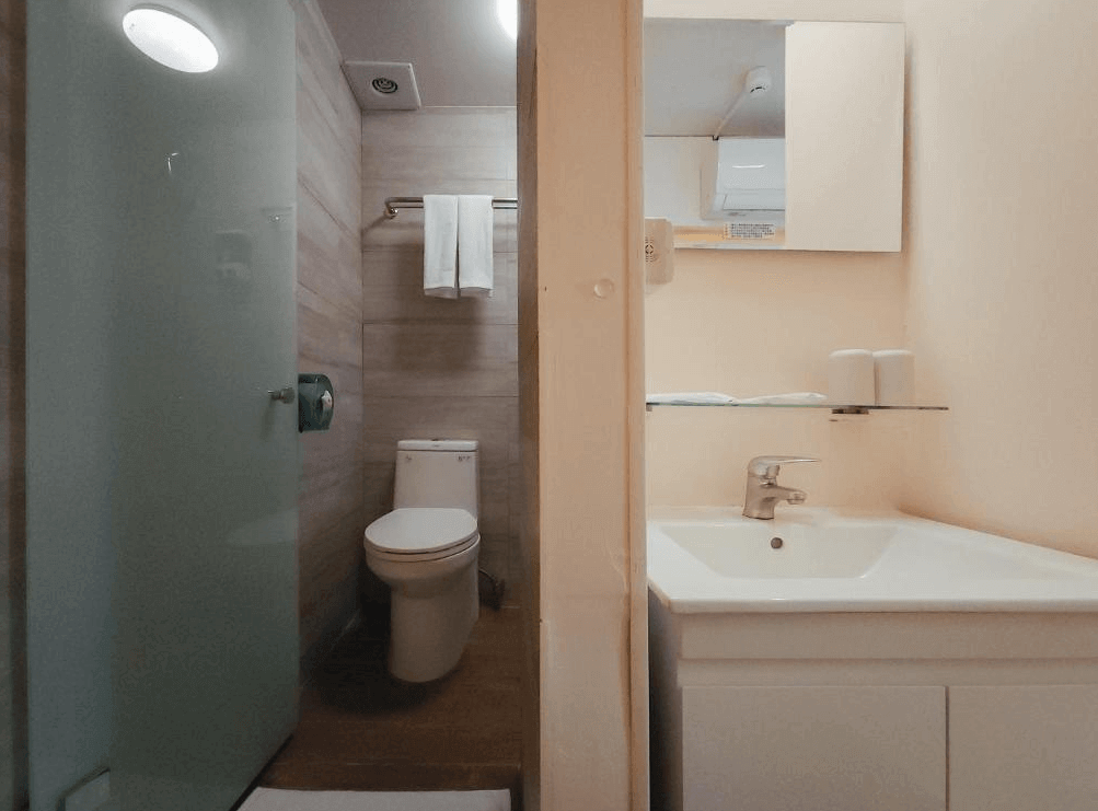 【台北車站青年旅館】Taipei Inn的私人衛浴空間內配有玻璃門淋浴間、現代馬桶與洗手台，淺木色磁磚與白色牆面營造出簡約清爽的風格，設備齊全且整潔衛生。