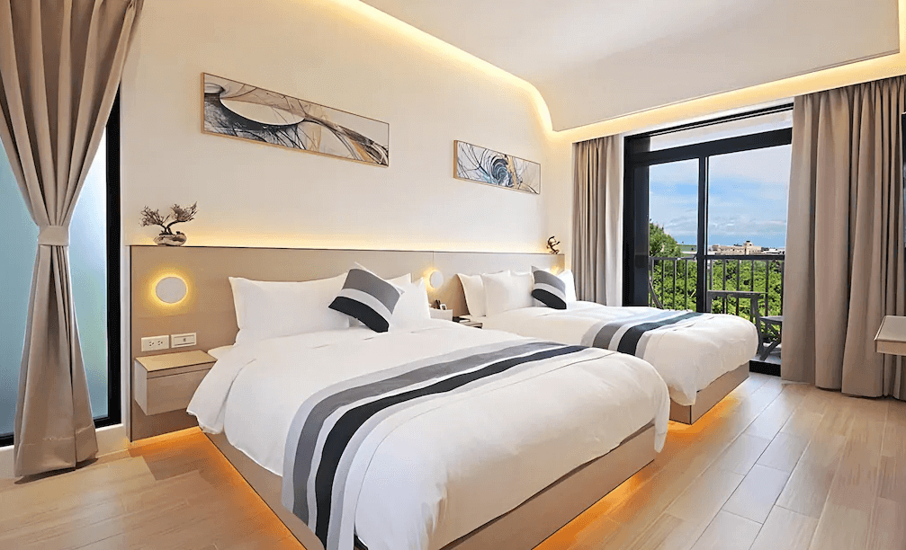 【綠島住宿】Unie會館的家庭房配置兩張大床，室內設計採用現代簡約風，搭配藝術掛畫與間接燈光，房間連接陽台，可欣賞戶外綠意與遠方海景。