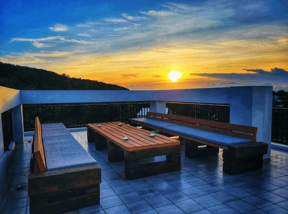 【綠島住宿】Unie會館的屋頂露天休憩區，設有木質長桌與沙發座位區，夕陽西下時分，天空與海平線交織出迷人景色，是欣賞夕陽的絕佳地點。