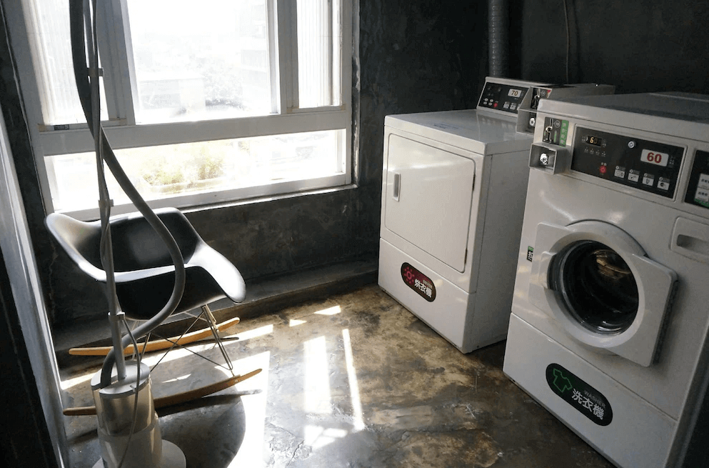 【台北車站青年旅館】WORK INN 北車館的洗衣區配有投幣式洗衣機與烘衣機，旁邊設有搖椅與大面窗戶，陽光灑落空間舒適，是長住旅客便利的生活設施之一。