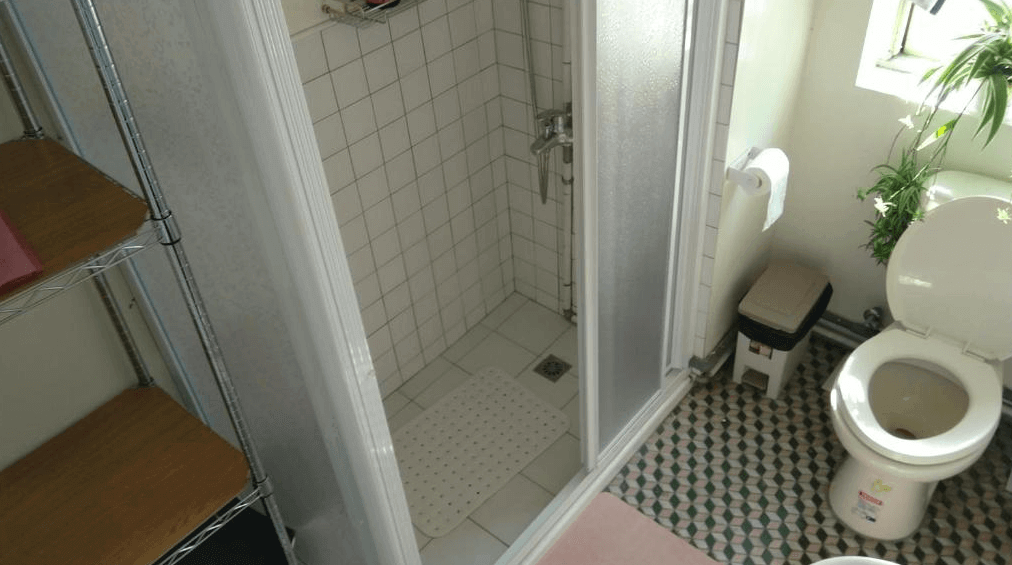 【左營住宿】丈引小院復古衛浴設備，衛浴空間設有小巧淋浴間、馬桶與自然採光窗戶，磁磚地板與金屬層架呈現簡樸老宅風格。