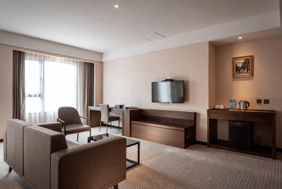 【一中街住宿】來來商旅的房間內部設有獨立客廳區，配有沙發組、書桌與牆掛電視，另備有茶水區與礦泉水，空間設計簡約大方，適合商務或家庭入住。