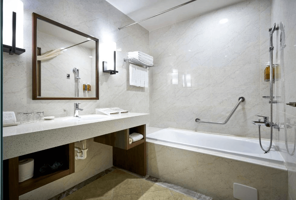 【一中街住宿】來來商旅的浴室空間，配備浴缸與淋浴設備，牆面為淺色大理石紋設計，洗手台寬敞附有鏡櫃與備品，另設有安全扶手提升便利性與安全性。