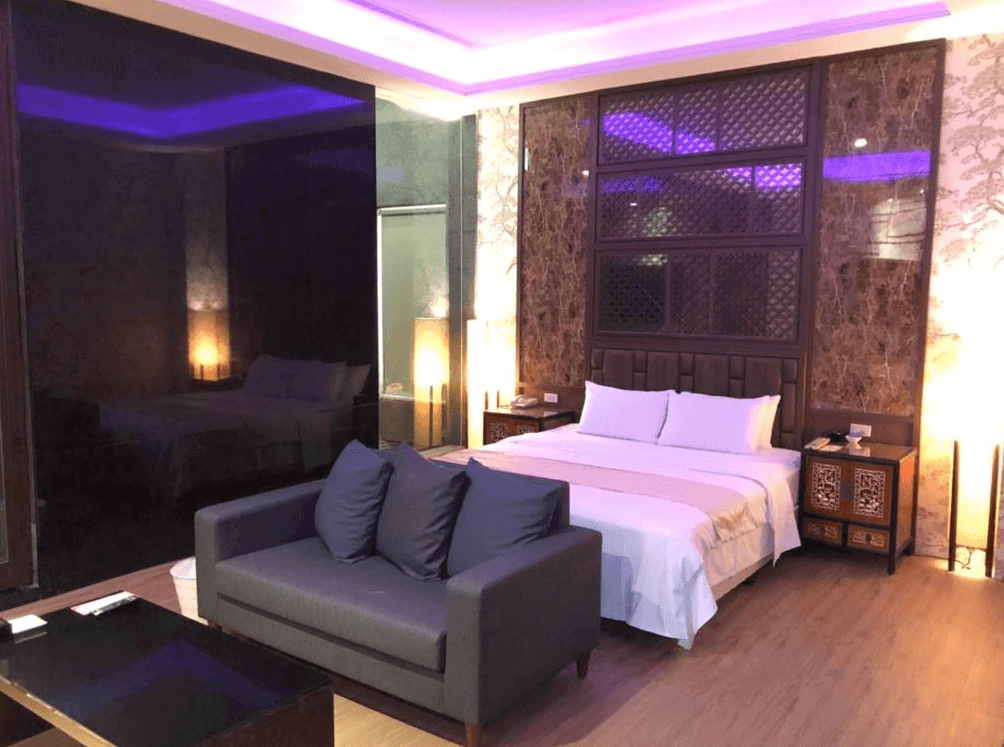 【楊梅住宿】依蝶時尚汽車旅館的雙人房，設有一張大床、深色沙發與玻璃茶几。房間燈光以紫色氛圍燈為主，營造浪漫氛圍，床頭牆面採用大理石與雕花木質裝飾，整體風格高雅。