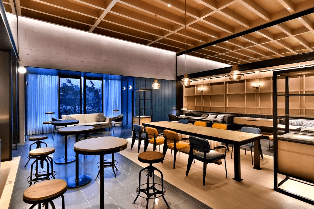 【台北寵物友善住宿】八里福朋喜來登酒店的共享空間，設有多樣桌椅組合與吊燈，牆面書櫃與沙發區提供放鬆或社交用途，整體空間明亮溫馨，適合旅客閱讀、工作與交誼。