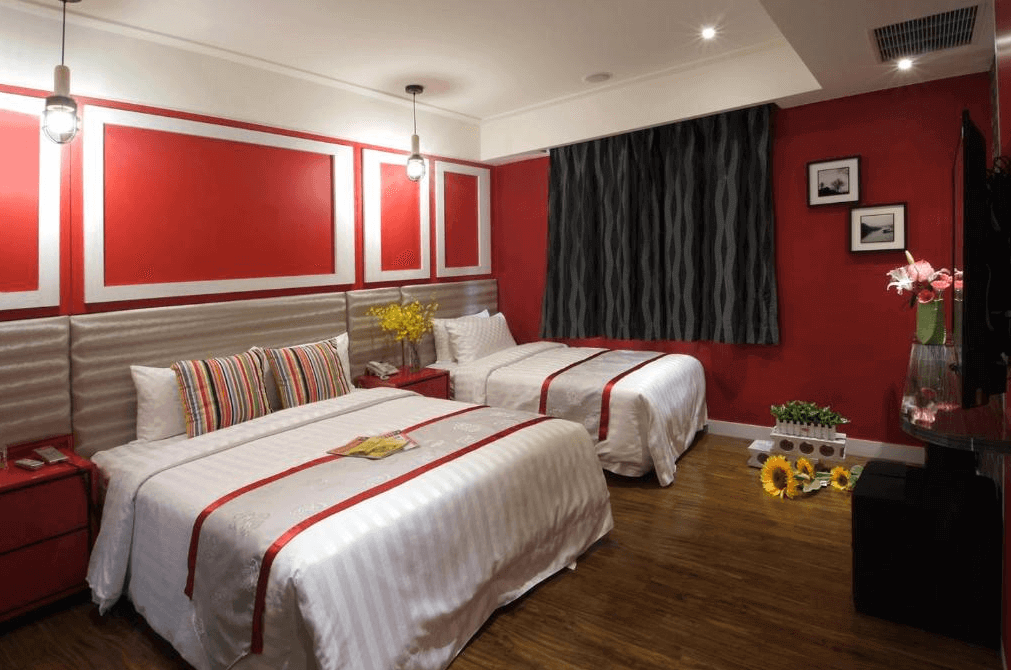 【楊梅住宿】凱萊汽車旅館的雙人房，以紅白配色為主，牆面與床頭板呼應，搭配一大一小床，適合親子入住。房內擺放向日葵與插花點綴，營造溫馨居家氛圍。