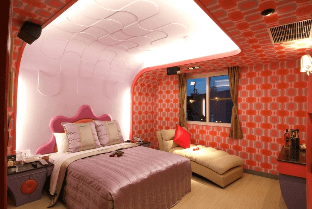 【楊梅住宿】凱萊汽車旅館的主題房型，牆面與天花板為紅色幾何花紋，搭配粉紫色床組與造型床頭，空間配置柔軟貴妃椅與燈光營造浪漫氛圍。