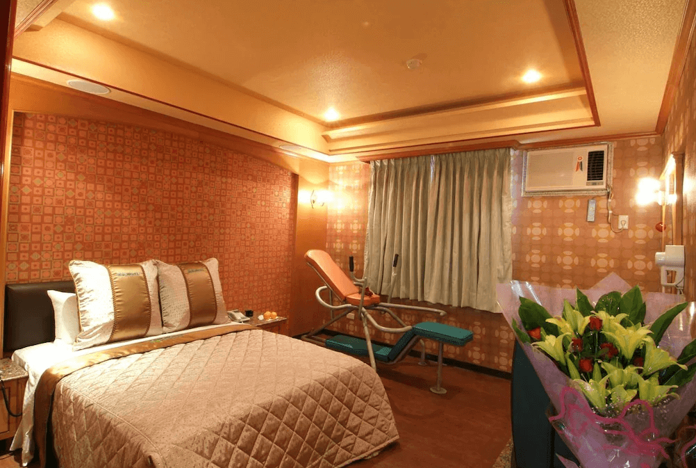 【楊梅住宿】凱萊汽車旅館的典雅房型，配有雙人床與特殊設計的情趣按摩椅，床頭與牆面為幾何圖樣裝飾，窗邊擺放花束增添浪漫感。