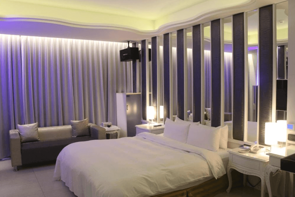 【龍潭住宿】凱虹汽車旅館的雙人房，設有一張大尺寸雙人床與金屬質感沙發，空間以紫藍間接照明與柔光打造浪漫氛圍。床頭背牆為多段式鏡面與軟墊立體設計，整體風格摩登且具情境感，適合情侶入住。