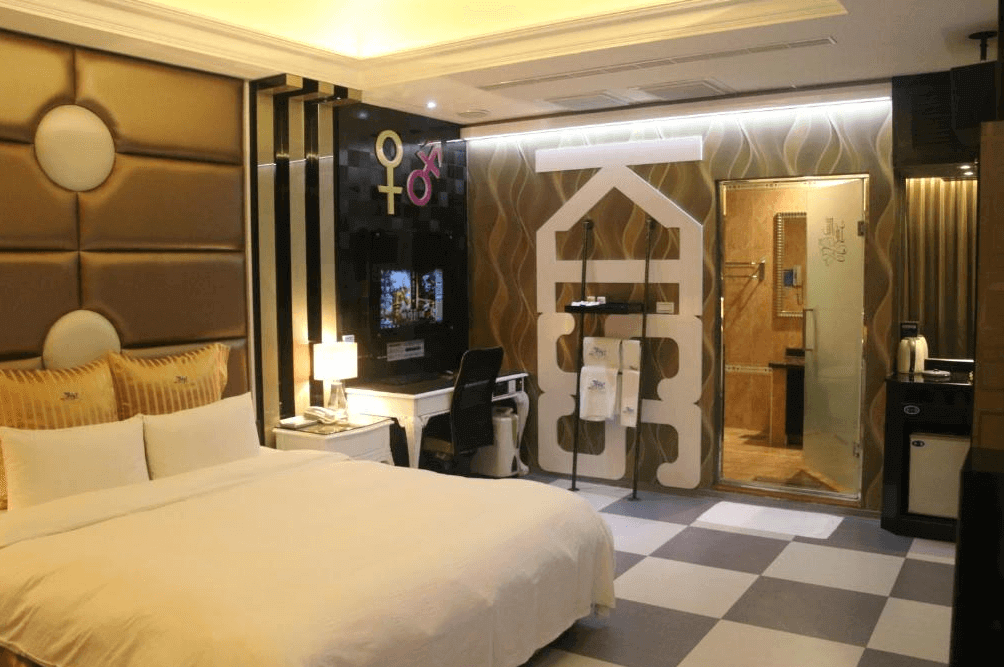 【龍潭住宿】凱虹汽車旅館的雙人套房，牆面飾有性別符號與大型「KISS」英文字樣，床頭為金色皮革包覆，營造奢華感。房內設有書桌、液晶電視及冰箱，乾濕分離浴室位於透明玻璃門後，整體風格前衛又具個性。