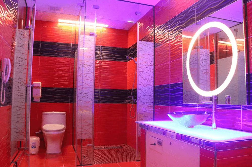 【龍潭住宿】凱虹汽車旅館的衛浴空間，以紅黑波紋磁磚鋪陳牆面與地板，搭配透明玻璃淋浴間與現代感洗手台。圓形LED鏡與紫光照明強化科技與夜店氛圍，營造出視覺衝擊感十足的沐浴體驗。