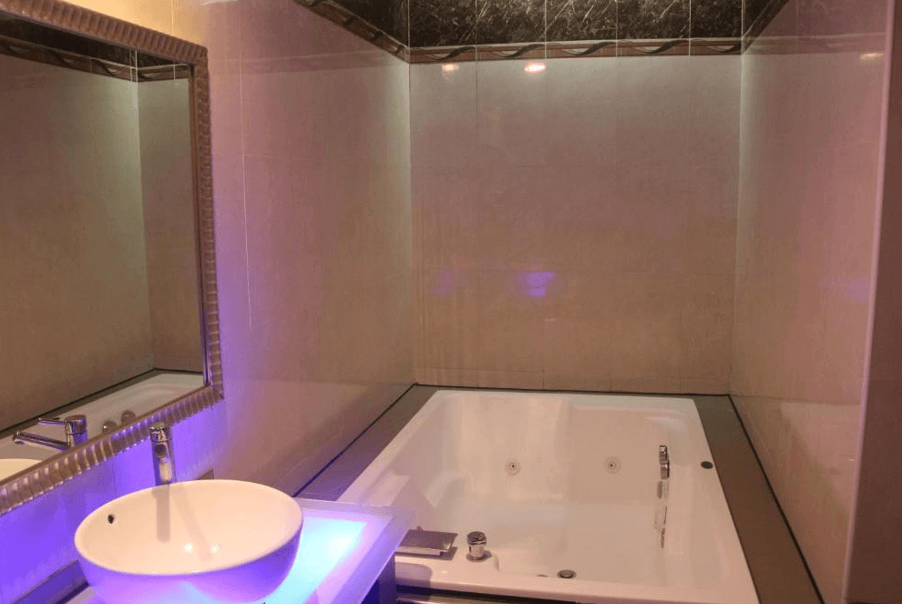 【龍潭住宿】凱虹汽車旅館的衛浴空間設有大型雙人按摩浴缸與獨立洗手台，牆面與地面為淺米色磁磚，搭配柔和間接燈光，打造出簡約卻放鬆的泡澡環境。浴缸上方設有大面鏡面，空間感倍增。