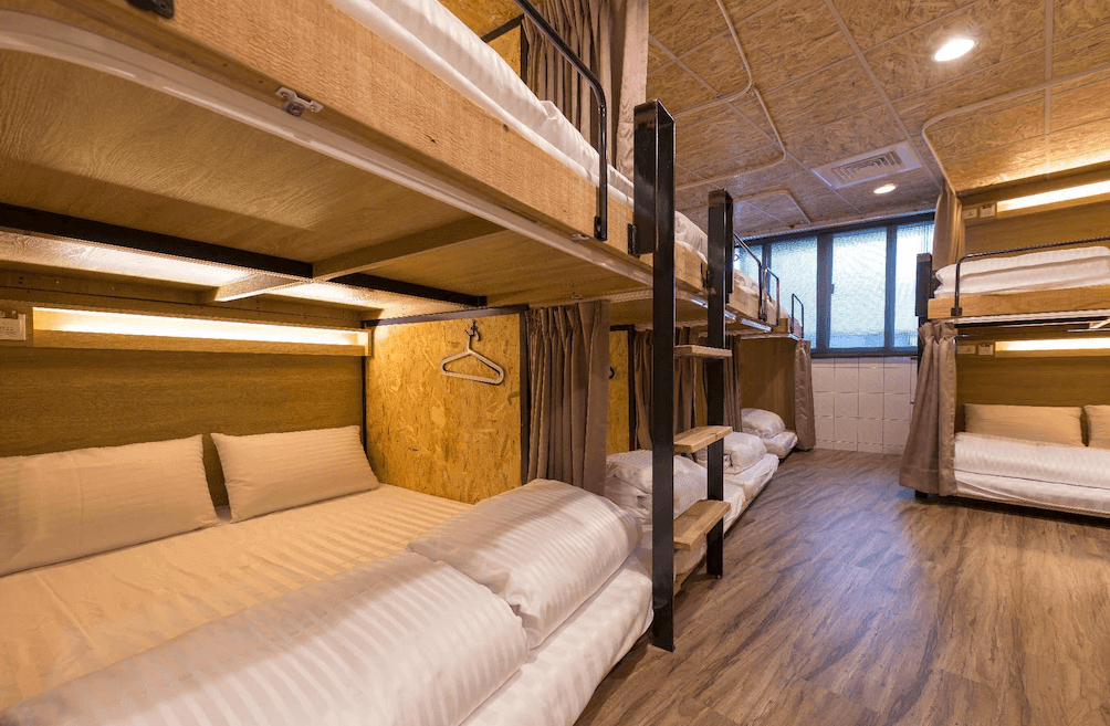 【台北車站青年旅館】北門窩泊旅的木質宿舍房，排列整齊的上下舖床位延伸至窗邊，柔和燈光營造出溫馨舒適的氛圍，適合背包客與團體旅客入住。