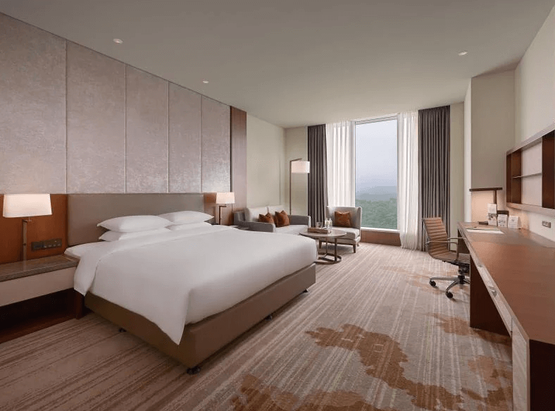 【台北寵物友善住宿】台北六福萬怡酒店的豪華客房，配有一張特大雙人床、辦公桌、舒適沙發區與全景落地窗，可眺望綠意盎然的戶外景色，室內風格簡約雅致。