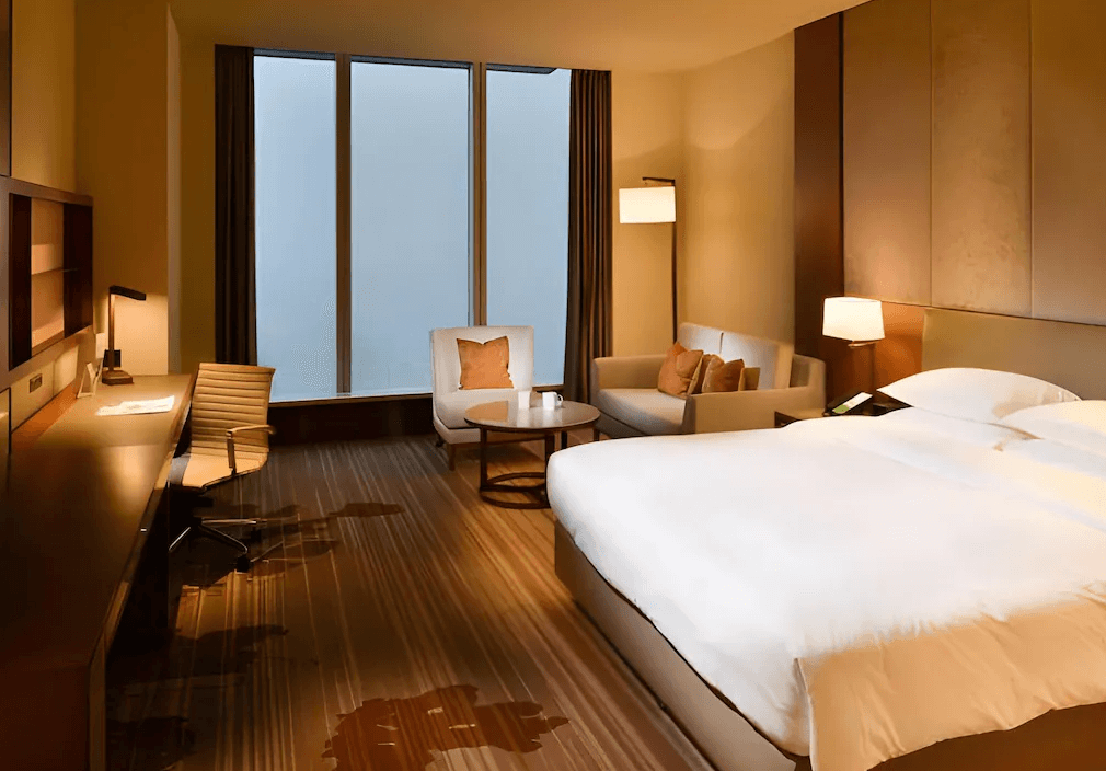 【台北寵物友善住宿】台北六福萬怡酒店的飯店客房，設有一張特大雙人床、辦公區與小型客廳空間，落地窗外霧氣瀰漫，營造靜謐沉穩的氛圍。