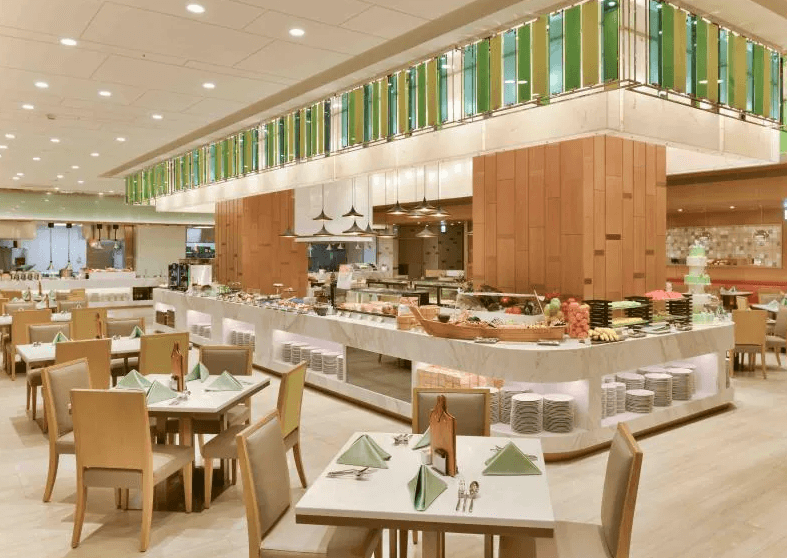 【台北寵物友善住宿】台北六福萬怡酒店的飯店自助餐廳，設有整排開放式取餐區與多樣美食擺盤，座位整齊配置，並配有綠色元素裝飾，營造清新舒適的用餐氛圍。