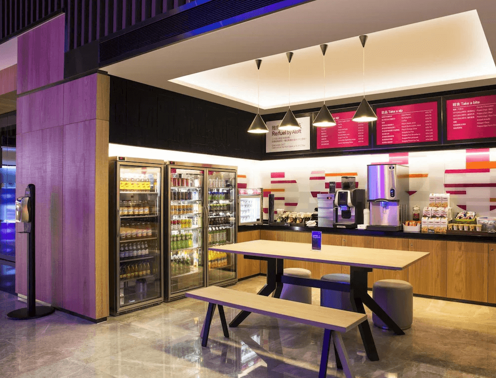 【台北寵物友善住宿】台北北投雅樂軒酒店的自助販售與咖啡區，陳列整排冷藏飲品與點心，設有咖啡機與用餐區，空間燈光明亮、色彩設計前衛，營造便利舒適的交流環境。