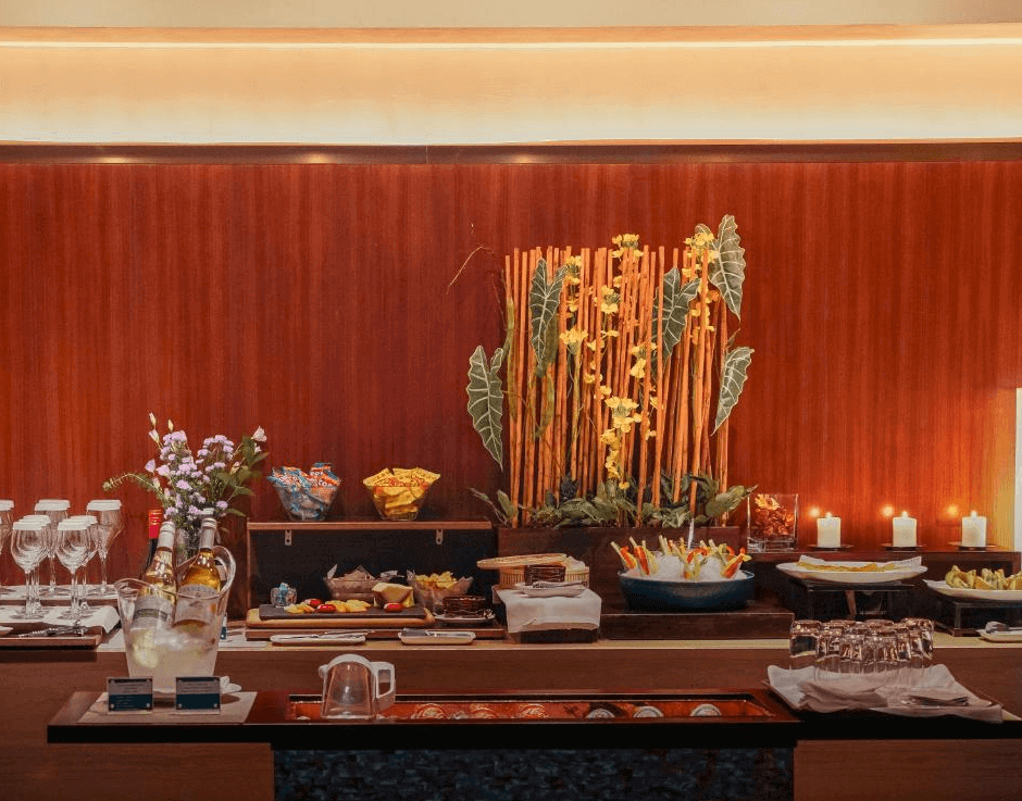 【台北小巨蛋住宿】台北商旅慶城館的自助吧檯區，備有紅白酒、果汁、甜點與輕食，裝飾以綠意植栽與溫暖木質牆面，氛圍雅致。