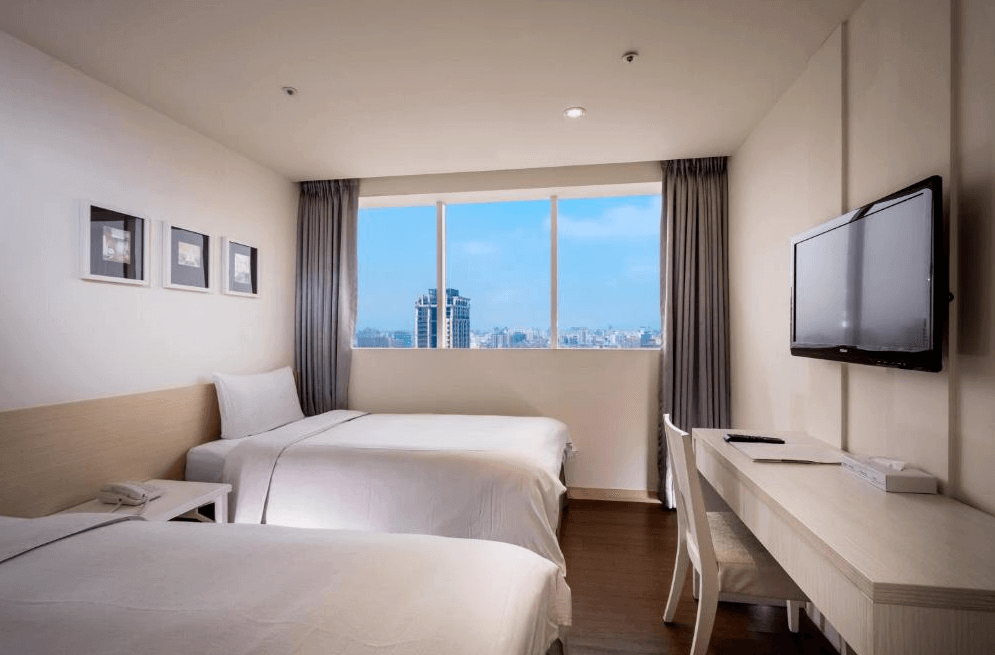 【三重住宿】台北薇米商旅的雙床房設計，採用白色與米色為主色調，搭配木質地板與大面窗景，可遠眺市區天際線。房內配有壁掛式電視、簡約書桌與兩張單人床，整體風格清爽舒適。