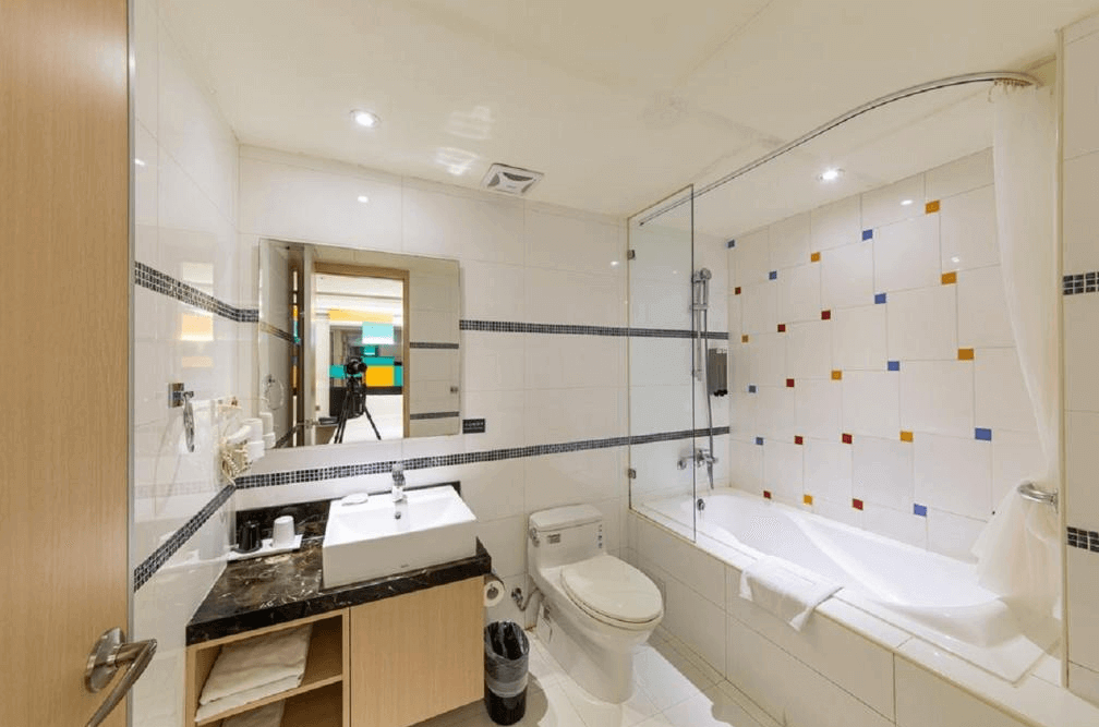 【蘆洲住宿】台北集賢商旅的衛浴空間，設有浴缸與蓮蓬頭，牆面為白色磁磚搭配彩色方形點綴。洗手台旁備有吹風機、毛巾與盥洗用品，功能齊全且乾淨整潔。