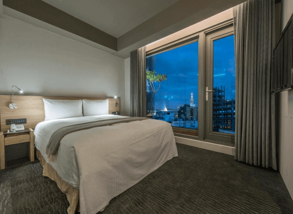 【台北小巨蛋住宿】台北馥華商旅敦北館的雙人房，設有大片窗景可遠眺台北夜色與地標建築，搭配柔和燈光與溫潤木質床頭設計。