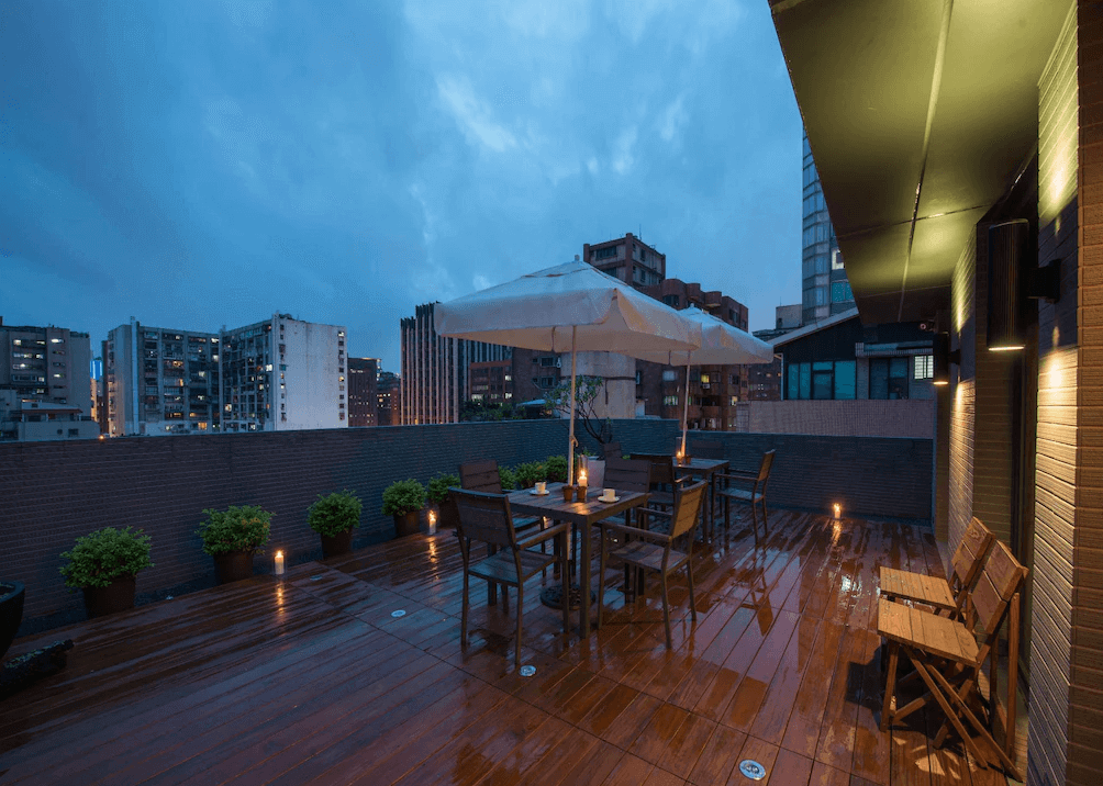 【台北小巨蛋住宿】台北馥華商旅敦北館的城市景觀露台，設有陽傘與戶外木質桌椅，傍晚點燈後氣氛溫馨，適合放鬆聊天與夜景欣賞。