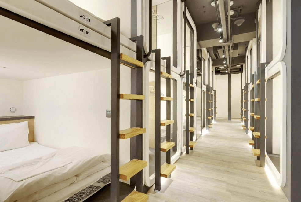 【台北車站青年旅館】台灣青旅膠囊旅店的雙層膠囊床位整齊排列於走道兩側，每個膠囊艙皆配有木質踏階與柔和燈光，整體空間乾淨明亮，營造出舒適的住宿氛圍。