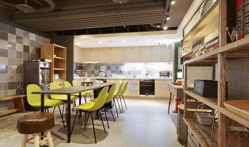 【台北車站青年旅館】台灣青旅膠囊旅店的共用廚房，配備完整烹飪設施與開放式櫥櫃，中央擺放長型餐桌與亮黃色椅子，空間寬敞明亮，是背包客交流與用餐的理想場所。