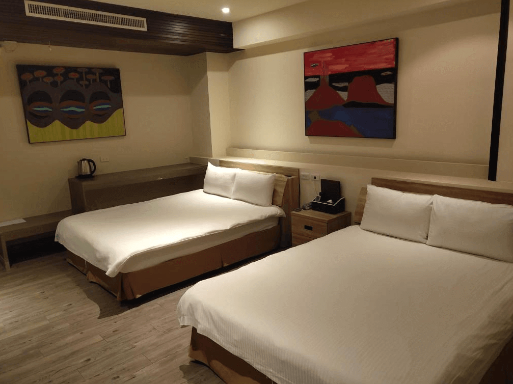 【楊梅住宿】君洋城堡的四人房，配有兩張雙人床，淺色牆面與木地板營造溫暖氛圍，牆上掛有抽象畫作點綴，房內備有電熱水壺與簡約書桌，適合家庭入住。