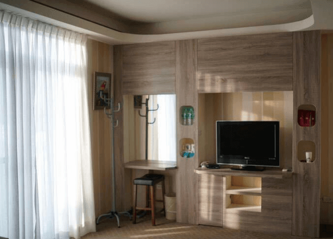 【楊梅住宿】君洋城堡的電視與梳妝區設計，淺木色櫃體結合開放式展示架與吊掛空間，電視下方設有儲物櫃，窗邊大片白色窗簾讓自然光透入，空間明亮整潔。