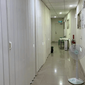 【左營住宿】國泰旅社內部走廊環境，長形走廊以白色牆面與摺疊門區隔房間，地板為亮面磁磚設計，並設有立扇與逃生出口標示，環境明亮整潔。