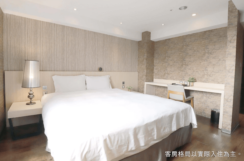 【一中街住宿】塔木德酒店一中館的雙人房，配有一張大床、柔和燈光與木質牆面，旁邊設有簡約的白色書桌與椅子，整體氛圍溫馨舒適。