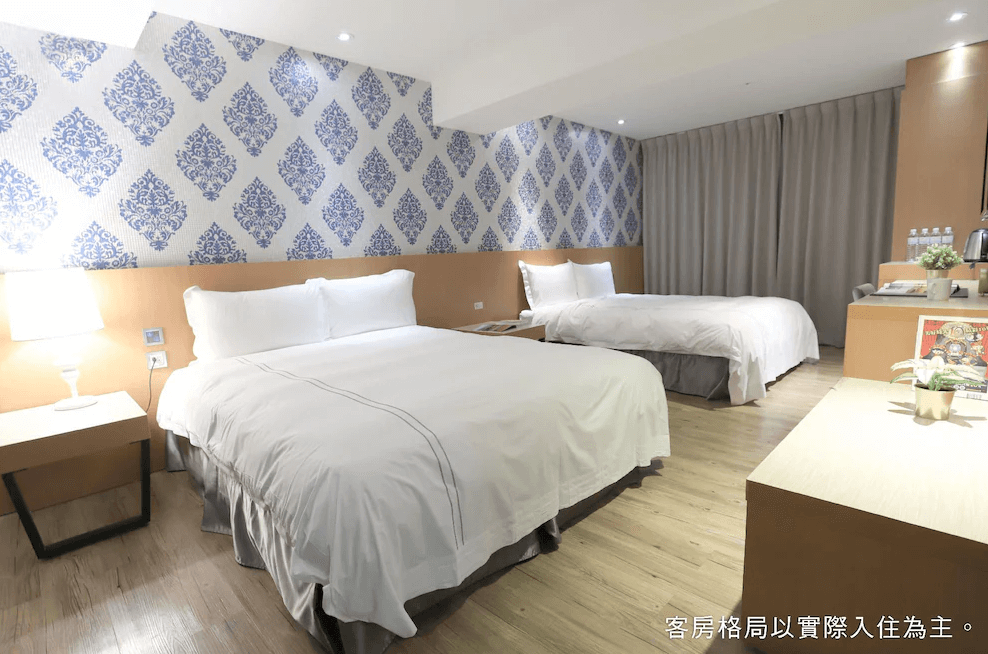 【一中街住宿】塔木德酒店一中館的四人房，設有兩張雙人床，牆面為藍白花紋壁紙，房內配備小桌子、瓶裝水與茶飲設備，適合家庭或朋友同住。