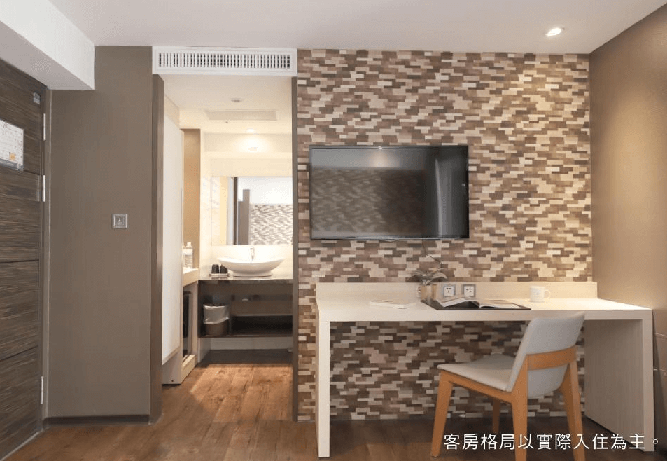 【一中街住宿】塔木德酒店一中館的房內設有牆掛式電視與書桌，書桌上擺放書本與杯子，後方為浴室入口，整體設計溫潤協調，營造舒適的居住氛圍。