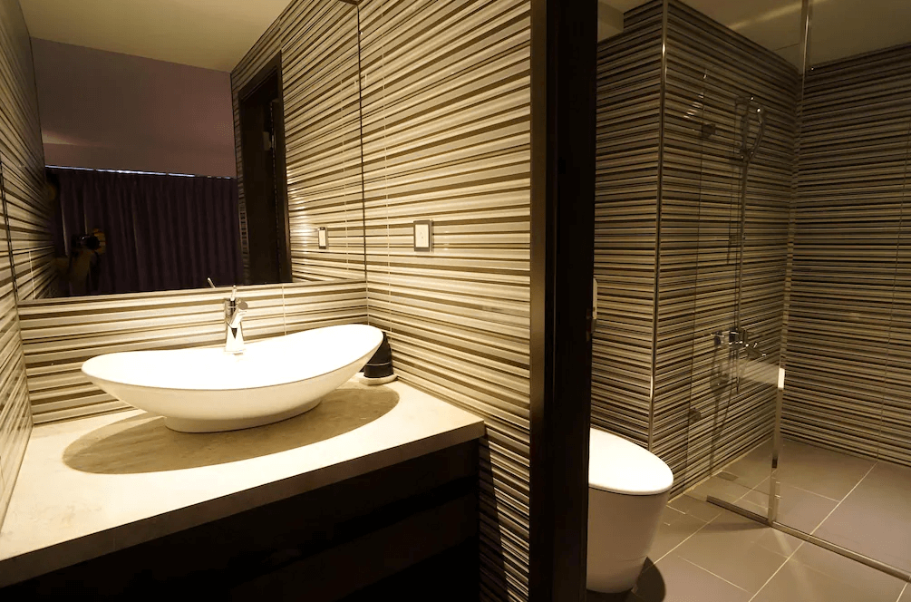 【一中街住宿】塔木德酒店一中館的浴室，牆面為灰白橫條紋設計，配有船型洗手台、馬桶與乾濕分離的淋浴間，空間乾淨明亮。