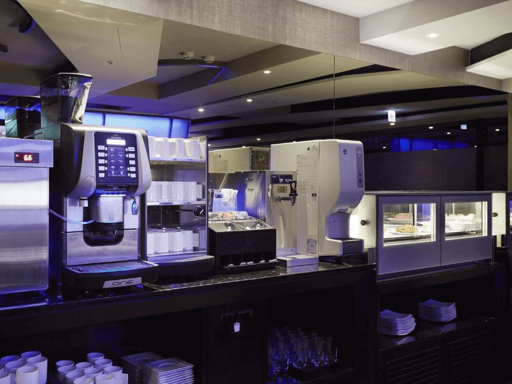 【台北小巨蛋住宿】天閣酒店 台北復興的自助餐區一景，配有多台咖啡與飲料機、餐盤與飲品備品整齊陳列，營造現代化餐飲空間。