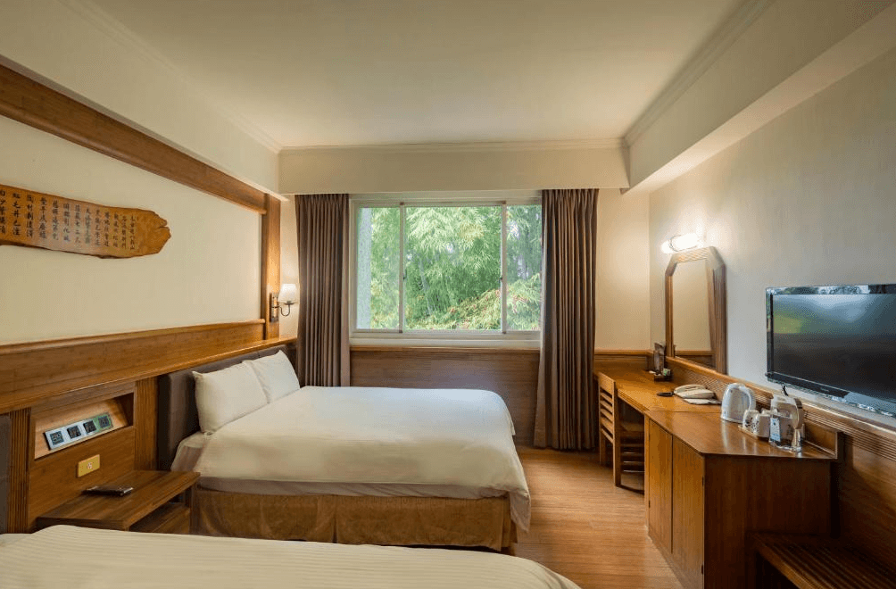 【杉林溪住宿】孟宗山莊大飯店的雙床客房，設有大片窗戶可眺望綠意景觀，房內配備書桌、化妝鏡、電視與熱水壺等設施。
