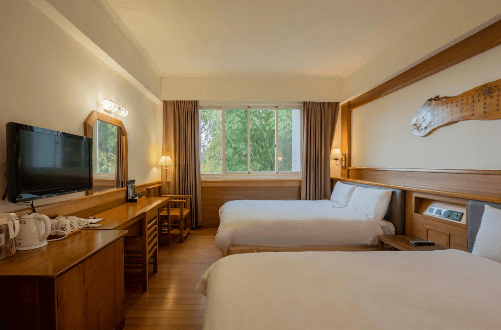 【杉林溪住宿】孟宗山莊大飯店的雙人雙床房，配有大片窗戶與自然光，房內備有梳妝桌、鏡子、電視與熱茶沖泡設備，展現溫馨質樸氛圍。