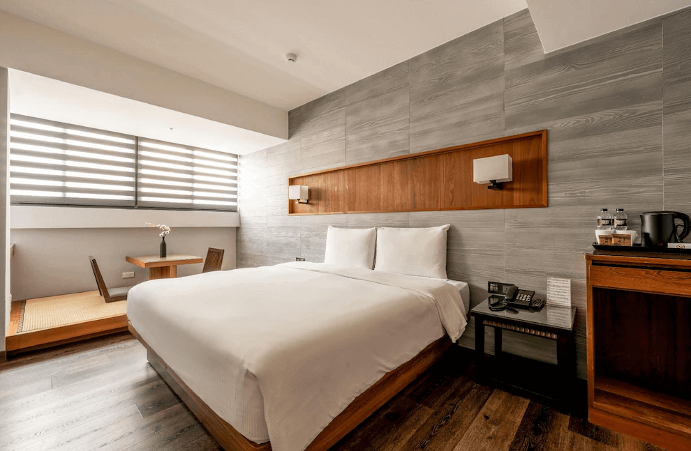 【一中街住宿】宿野行旅的日式簡約風格雙人房，設有一張大床與木質牆面裝飾，窗邊鋪設榻榻米與原木茶几，空間沉穩溫暖，並提供礦泉水與熱水壺備品。