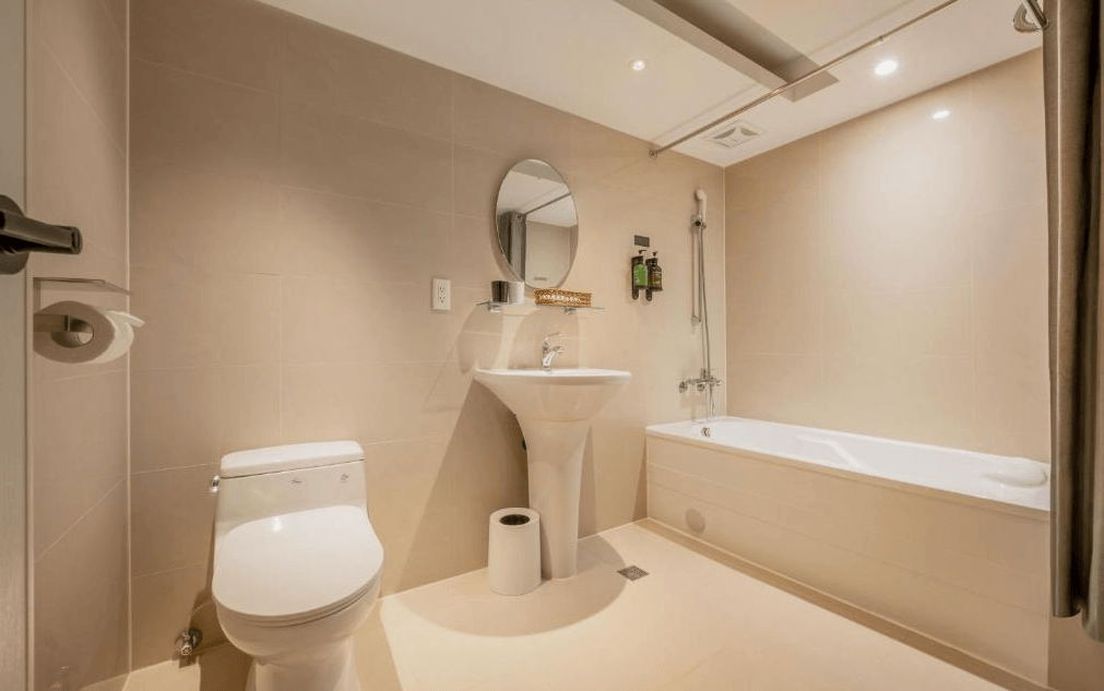【一中街住宿】宿野行旅的浴室空間明亮潔淨，牆面與地板為溫潤米色調，設有浴缸與淋浴兩用設備、洗手台與鏡子，提供基本備品與壁掛洗沐用品。