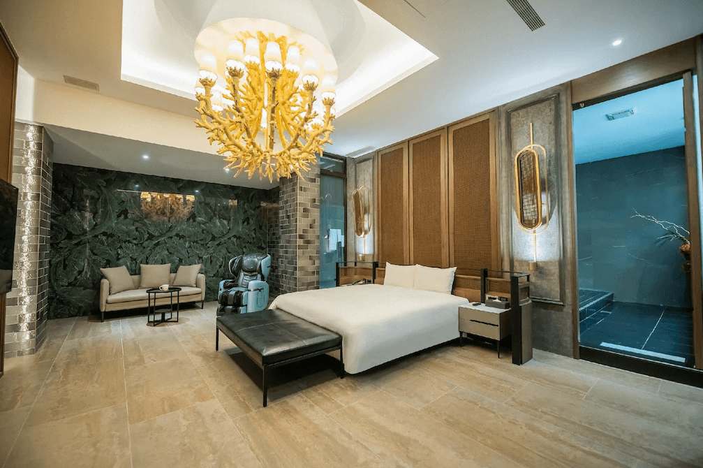 【草屯住宿】山月景緻旅館的豪華套房，設有一張大型雙人床、按摩椅、沙發休息區，牆面採用深綠色植物圖樣設計，搭配金色吊燈與暖色系燈光，右側為私人湯屋空間，整體高雅大器。