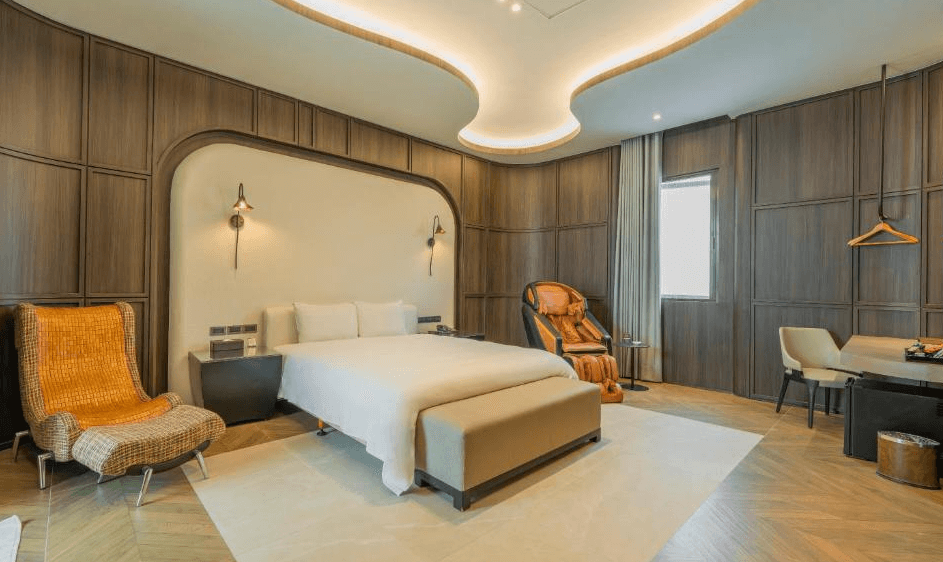 【草屯住宿】山月景緻旅館的雙人房，中央為一張舒適雙人床，右側配置高級按摩椅與簡約工作桌，左側為藤編造型休閒椅，天花板曲線設計搭配間接照明，營造柔和寧靜氛圍。